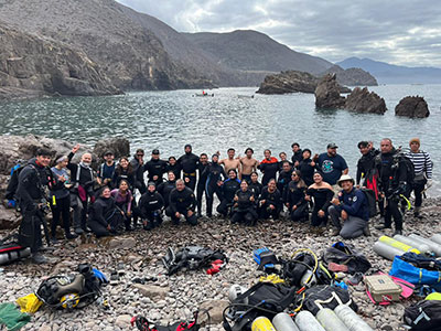 A group of divers and marine conservation volunteers on a rocky beach after reef survey